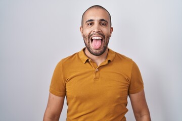 Fototapeta premium Hispanic man with beard standing over white background sticking tongue out happy with funny expression. emotion concept.