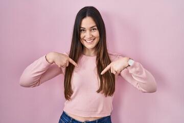 Young brunette woman standing over pink background looking confident with smile on face, pointing oneself with fingers proud and happy.