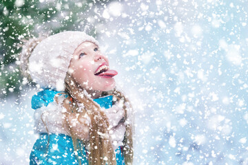 A little girl puts out tongue to catch snowflakes on snowfall weather.