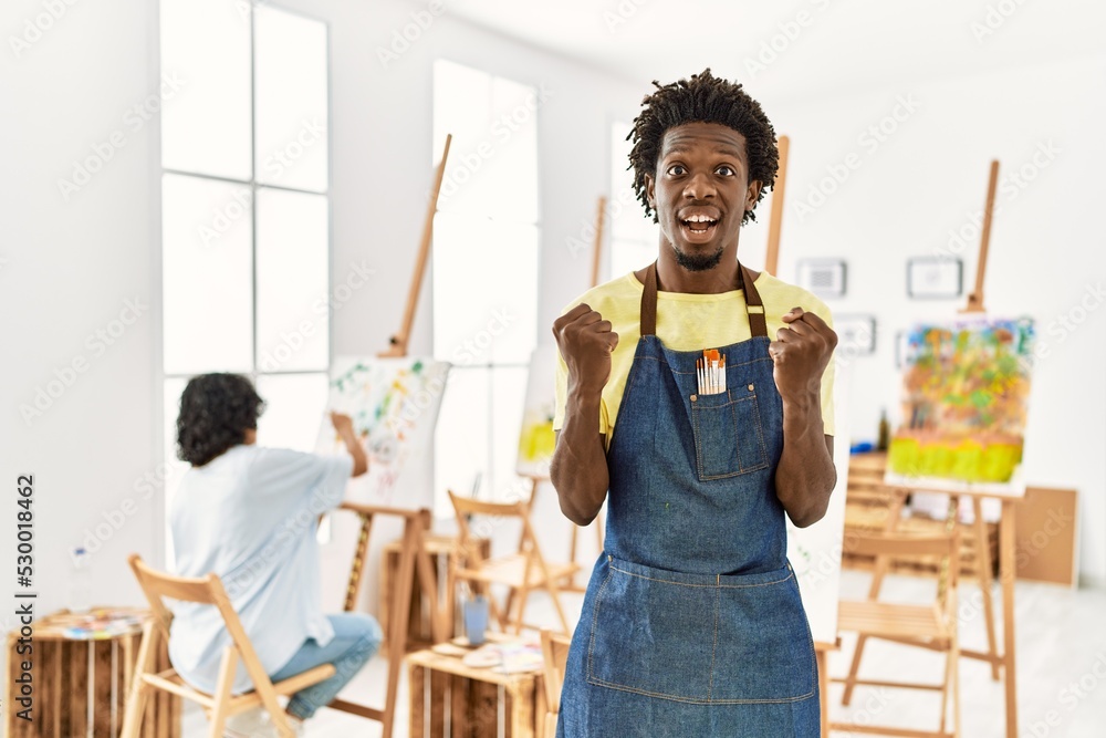 Sticker African young man standing at art studio celebrating surprised and amazed for success with arms raised and open eyes. winner concept.