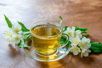cup of jasmine tea and tea leaves on a wooden table next to jasmine sprigs with leaves and flowers, herbal tea healing diet