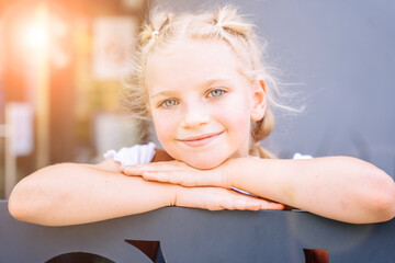 Blond schoolgirl back to school after summer vacations. Child chin on her hands, pensively looking at camera. Lifestyle portrait of lLittle caucasian girl seven years old elementary school.