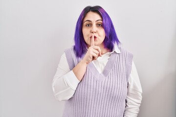 Plus size woman wit purple hair standing over white background asking to be quiet with finger on lips. silence and secret concept.