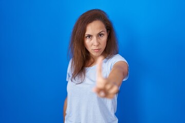 Fototapeta premium Brunette woman standing over blue background pointing with finger up and angry expression, showing no gesture