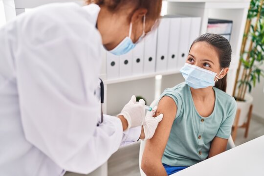 Woman and girl doctor and patient wearing medical mask vaccinating arm at clinic