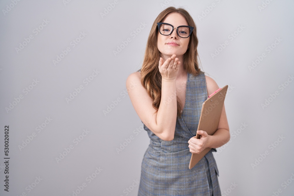 Poster caucasian woman wearing glasses and business clothes looking at the camera blowing a kiss with hand 