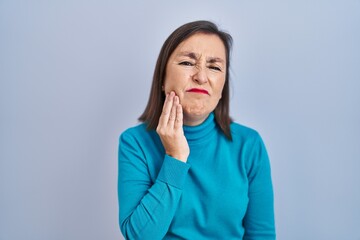 Middle age hispanic woman standing over isolated background touching mouth with hand with painful expression because of toothache or dental illness on teeth. dentist