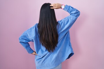 Young asian woman standing over pink background backwards thinking about doubt with hand on head