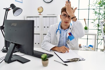 Obraz premium Young caucasian doctor man working at the clinic surprised with hand on head for mistake, remember error. forgot, bad memory concept.