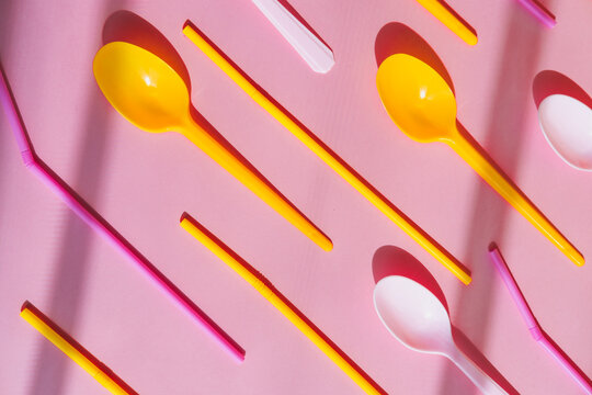 Plastic disposable pink and yellow ice cream spoons on a bright background with shadows.