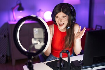 Young caucasian woman playing video games recording with smartphone celebrating victory with happy smile and winner expression with raised hands