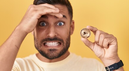 Handsome hispanic man holding uniswap cryptocurrency coin stressed and frustrated with hand on head, surprised and angry face