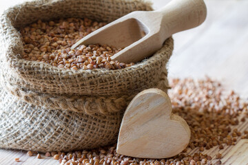 Buckwheat in jute sack with heart of wood on wooden background, healthy heart food concept  - obrazy, fototapety, plakaty