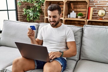 Young hispanic man smiling confident using laptop and credit card at home