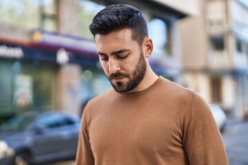 Young hispanic man with relaxed expression standing at street