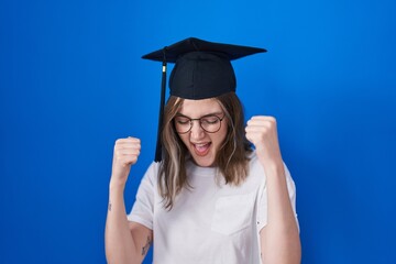 Blonde caucasian woman wearing graduation cap very happy and excited doing winner gesture with arms raised, smiling and screaming for success. celebration concept.