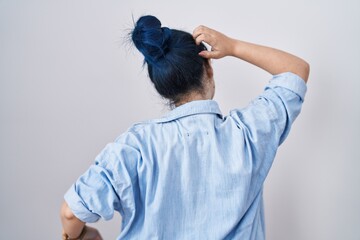 Young modern girl with blue hair standing over white background backwards thinking about doubt with hand on head