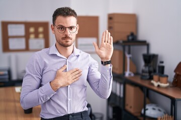 Young hispanic man at the office swearing with hand on chest and open palm, making a loyalty promise oath