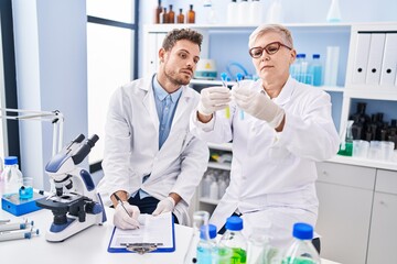 Fototapeta premium Mother and son scientist partners holding test tubes writing on clipboard at laboratory