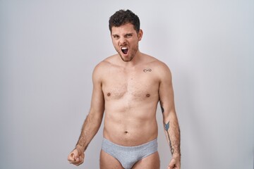 Fototapeta premium Young hispanic man standing shirtless wearing underware angry and mad screaming frustrated and furious, shouting with anger. rage and aggressive concept.