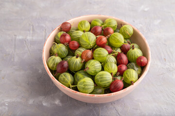 Fresh red and green gooseberry in ceramic bowl on gray concrete, side view.