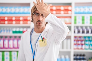 Caucasian man with mustache working at pharmacy drugstore surprised with hand on head for mistake,...