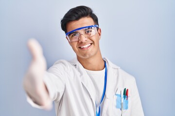 Fototapeta premium Hispanic man working as scientist smiling friendly offering handshake as greeting and welcoming. successful business.