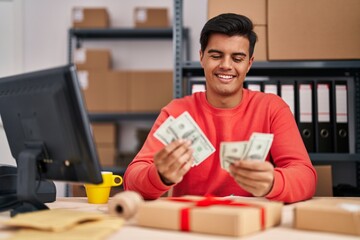 Young hispanic man ecommerce business worker using laptop counting dollars at office