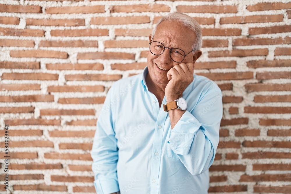 Sticker Senior man with grey hair standing over bricks wall looking stressed and nervous with hands on mouth biting nails. anxiety problem.