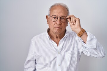 Senior man with grey hair holding glasses with hand thinking attitude and sober expression looking self confident