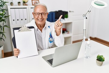 Senior doctor man holding clipboard with blank space smiling happy pointing with hand and finger to the side