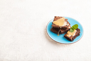 Chocolate brownie with caramel sauce on gray concrete, side view, copy space.