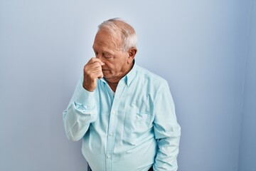 Senior man with grey hair standing over blue background tired rubbing nose and eyes feeling fatigue...