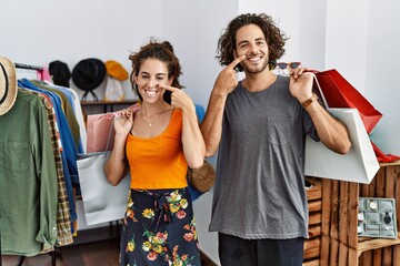 Young hispanic couple holding shopping bags at retail shop pointing with hand finger to face and nose, smiling cheerful. beauty concept