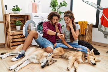 Young hispanic couple doing laundry with dogs looking at the watch time worried, afraid of getting late