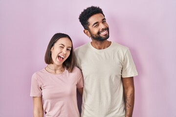 Young hispanic couple together over pink background winking looking at the camera with sexy...