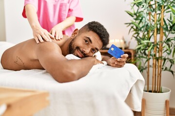 Obraz na płótnie Canvas Young african american reciving back massage and holding credit card at beauty center.