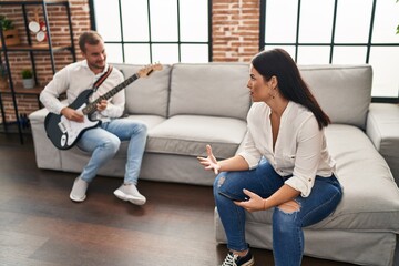 Man and woman couple smiling confident playing guitar at home