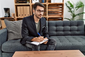Young hispanic man having psychology session writing on checklist at clinic