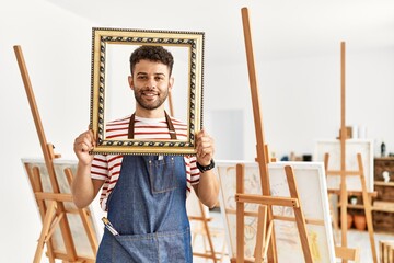 Young arab artist man smiling happy holding empty frame at art studio.