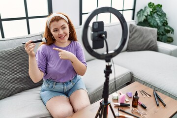Fototapeta na wymiar Young redhead woman recording make up tutorial with smartphone at home smiling happy pointing with hand and finger