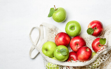 red and green apples in a mesh bag on a light background, top view