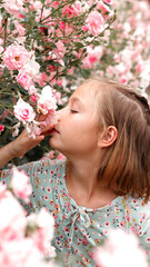 Young Girl Smelling Rose Flower Over Blooming Bushes In Garden Outdoor