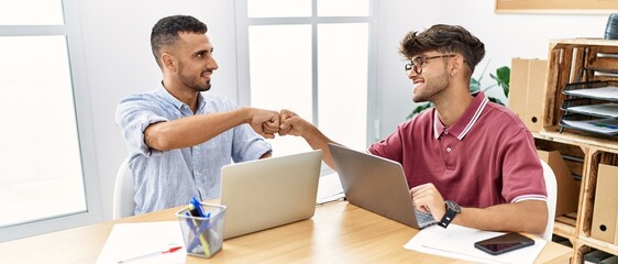 Two business workers smiling happy bump fists at the office.