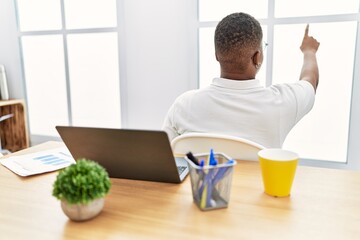 Young african man working at the office using computer laptop posing backwards pointing ahead with finger hand