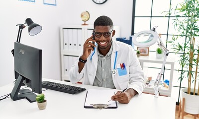 Young african american man wearing doctor uniform talking on the smartphone at clinic