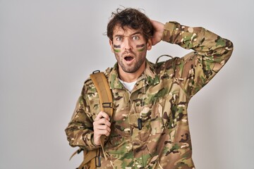 Hispanic young man wearing camouflage army uniform crazy and scared with hands on head, afraid and surprised of shock with open mouth