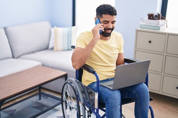 Young arab man talking on smartphone sitting on wheelchair at home