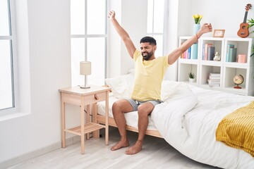 Obraz na płótnie Canvas Young arab man waking up stretching arms at bedroom