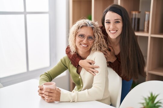 Two women mother and daughter hugging each other drinking coffee at home
